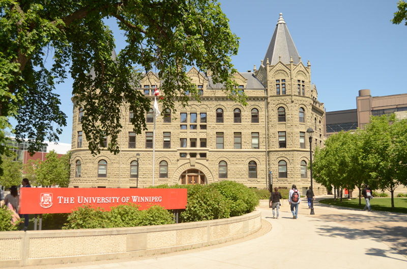 Photo of the University of Winnipeg's Portage Avenue entrance on a sunny day in the summer with students walking up to the doors