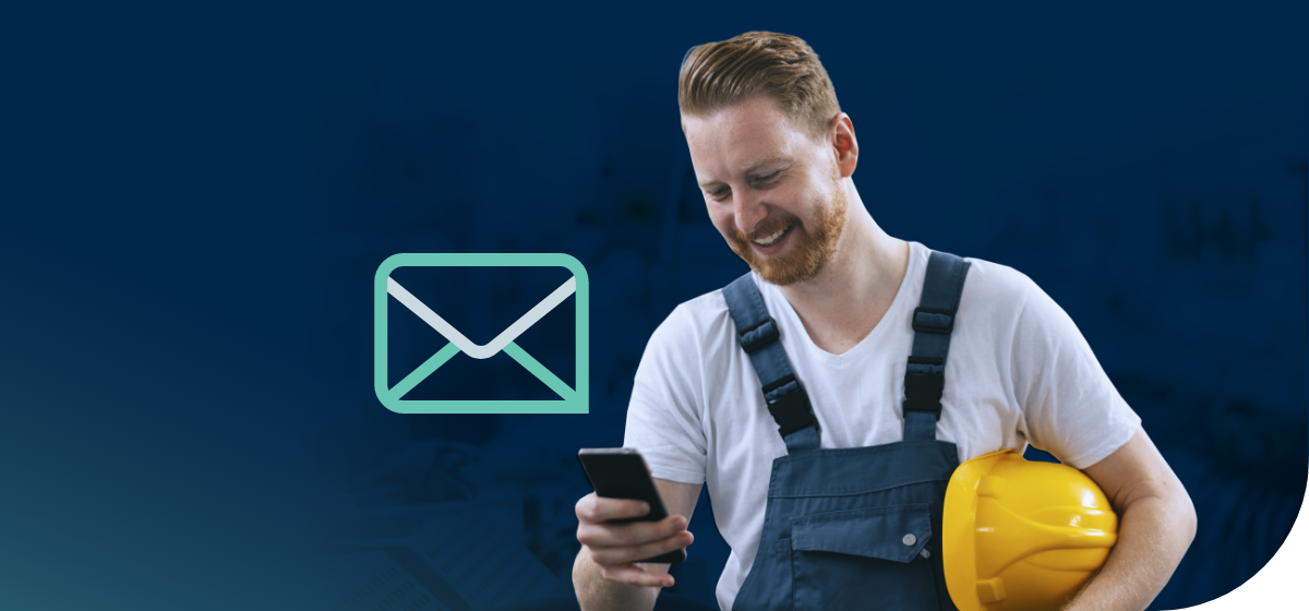 A smiling male journeyperson holding a yellow safety helmet under his arm while he sends an email on his smartphone with his other hand. A graphic outline of a envelope floats in the blue background behind him.