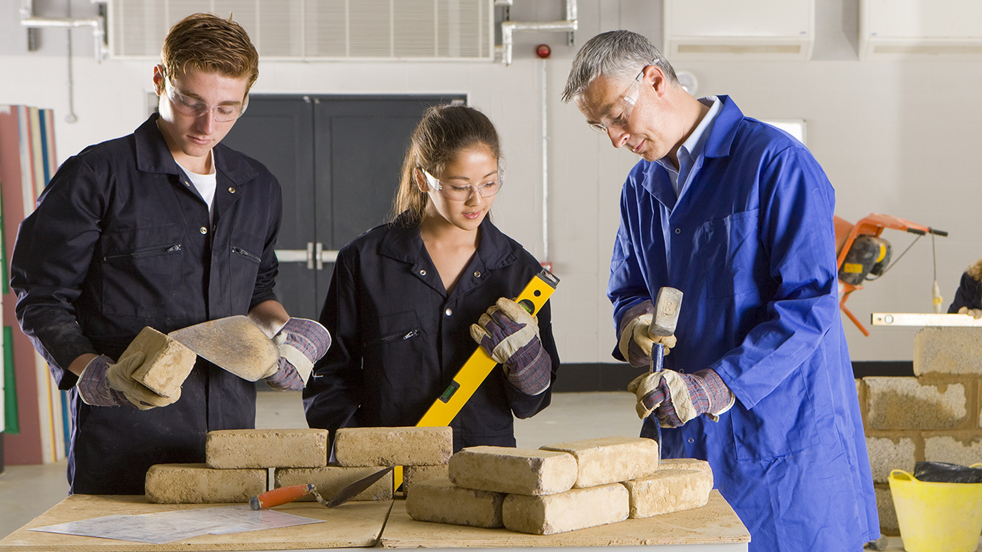 a male Bricklayer journeyperson instructor showing a male and female students how to use various tools as part of their pre-employment training.