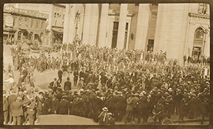 A large crowd of people standing in the middle of Portage Ave and Main St in Winnipeg, 1919. A building in the background reads: Spencer Heater Co of Canada Ltd. Spencer Self-Feed Steam and Hot Water Boilers. Western Gem Coal.