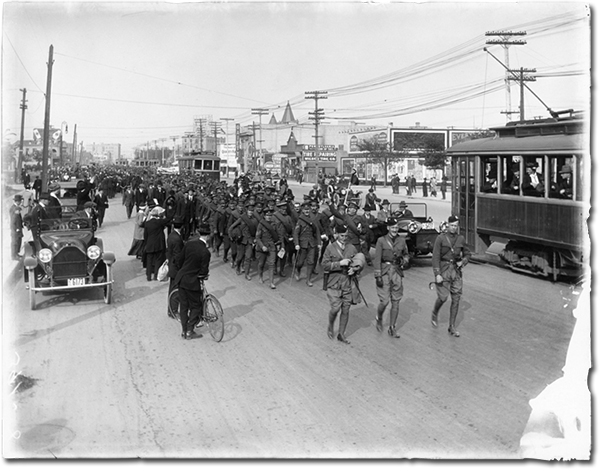 Photo of a parade of soldiers marching down Portage Ave in 1915, while a crowd of people watch