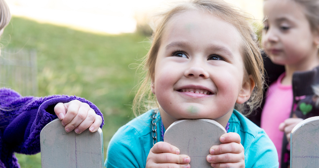 Young girl smiling and looking over the top of a fence