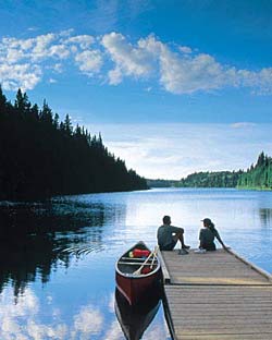 Un couple assis sur un quai près d’un lac et d’un canoë qui profite de l’été chaud du Manitoba